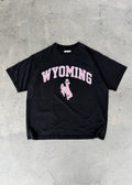 Faded Black + Rose | Black t-shirt with 'Wyoming' printed in pink on a concrete floor