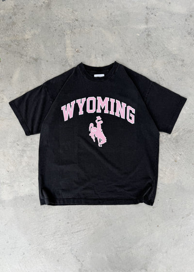 Faded Black + Rose | Black t-shirt with 'Wyoming' printed in pink on a concrete floor