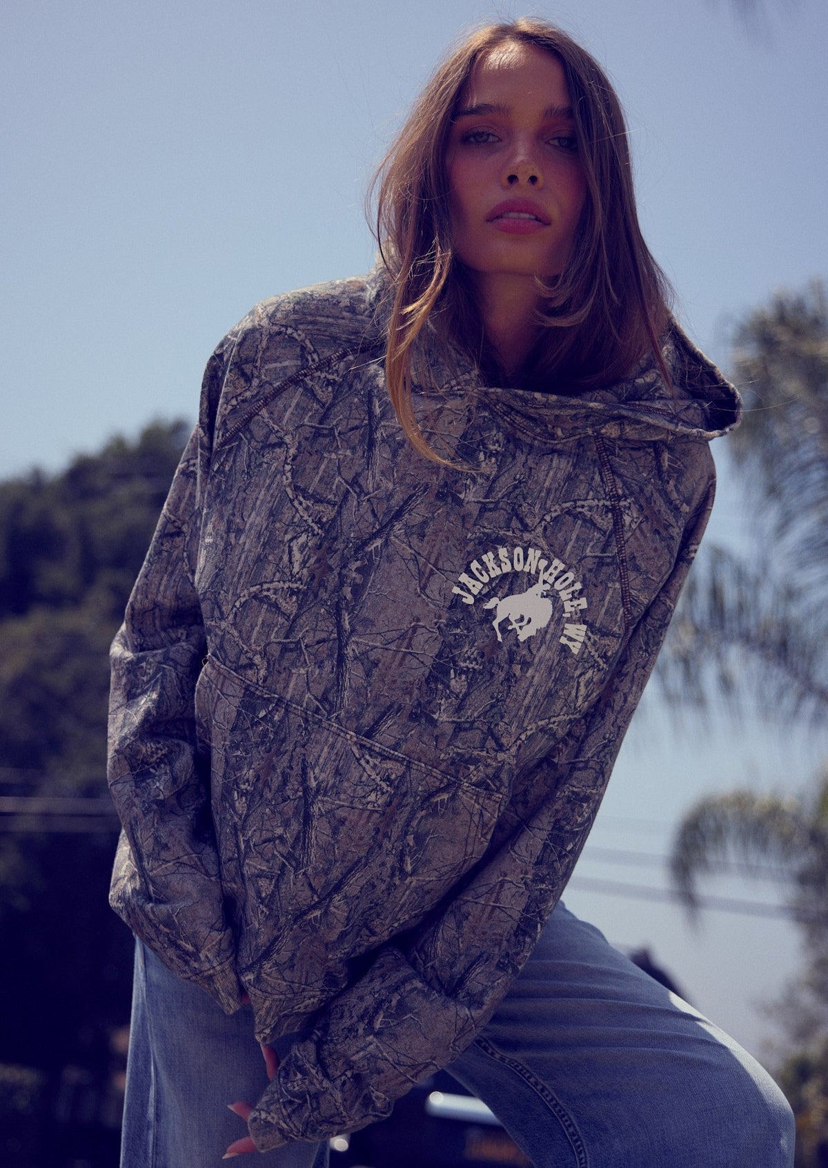 Sage Brush Camo | Person wearing a patterned hoodie with a logo outdoors