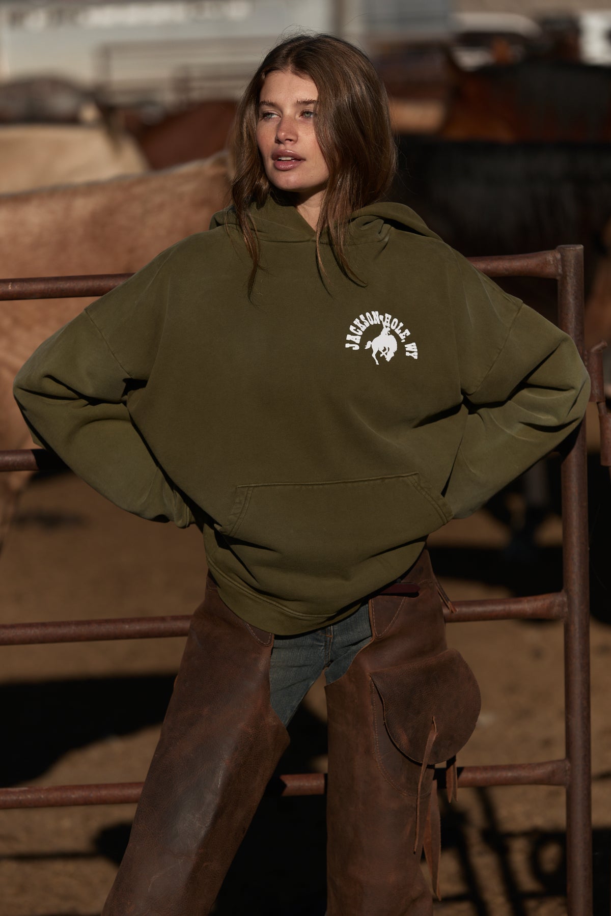 Army Green | Person wearing an olive green hoodie with a logo, standing in front of a rustic background.