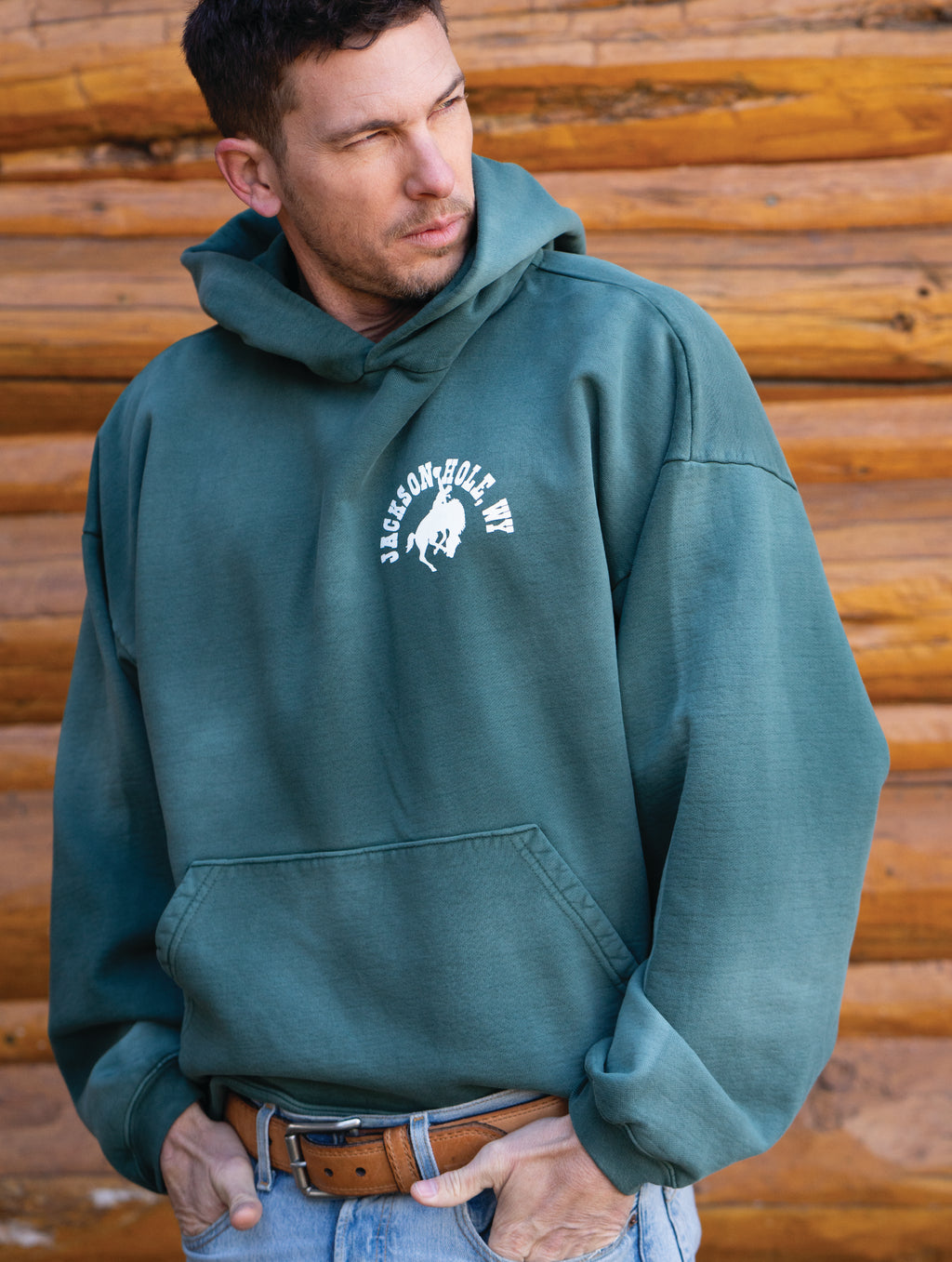 Sun Faded Green | Man wearing a green hoodie with a logo in front of a wooden background