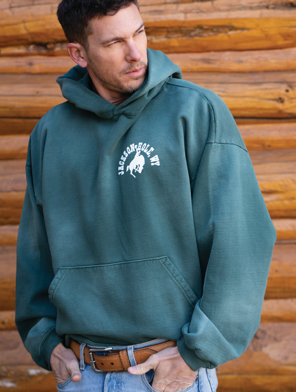 Sun Faded Green | Man wearing a green hoodie with a logo in front of a wooden background